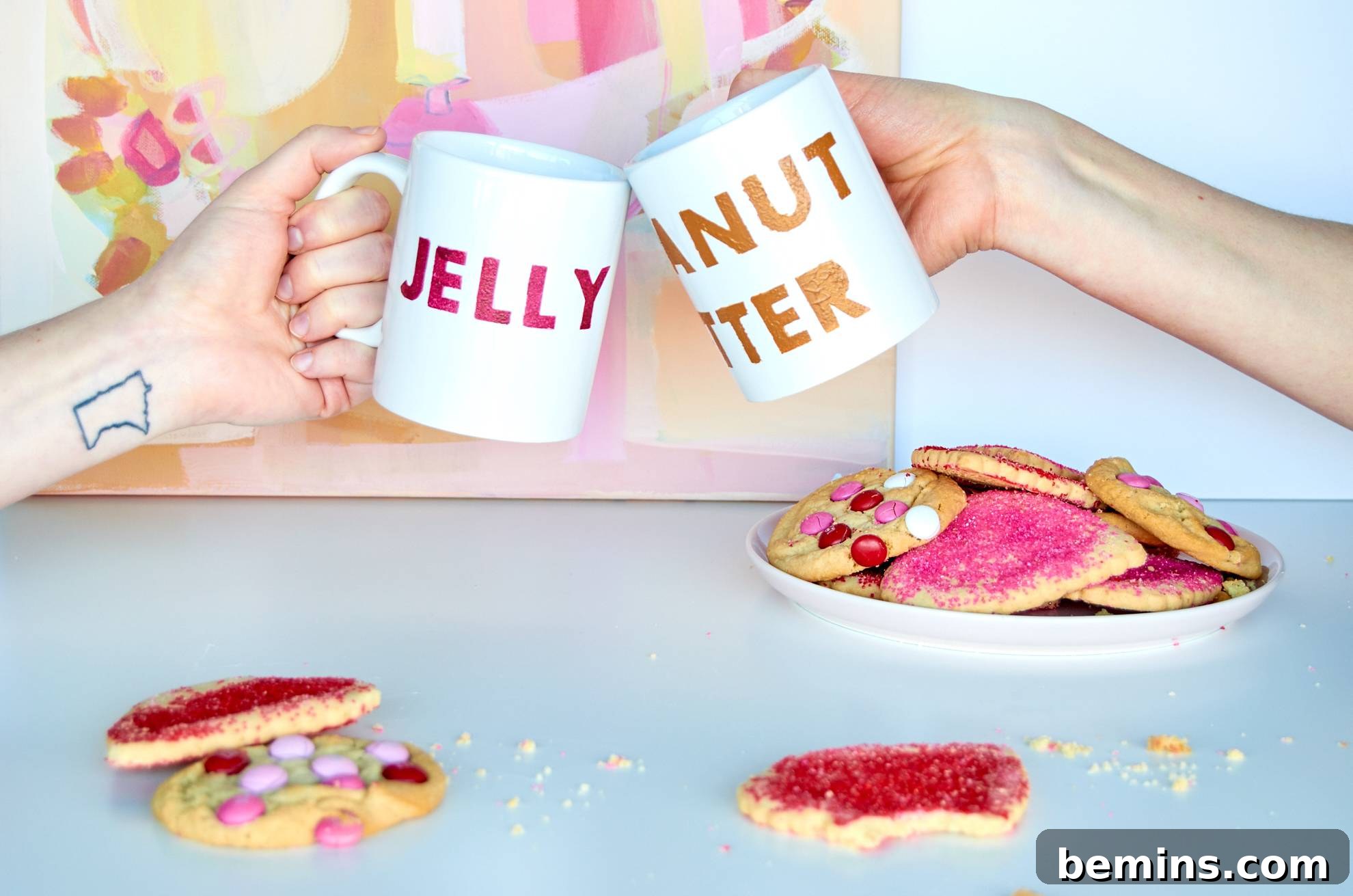 Two women cheers using their decorative mugs over a plate of sugar cookies.