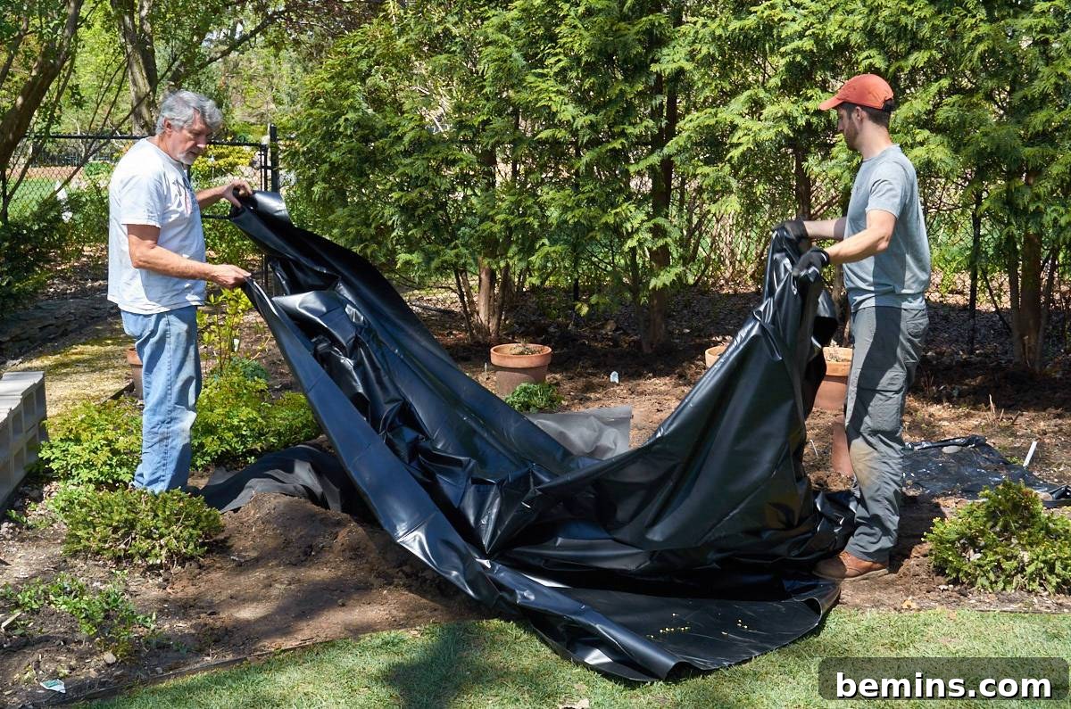Two men positioning the black pond liner into the excavated pond hole.