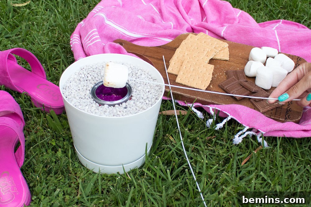 Campfire Not Required: Your Portable S'mores Fire Pot Solution 2 Hand holding a toasted marshmallow over a homemade s'mores fire pot, set up on a patio table, ready for a delicious treat.