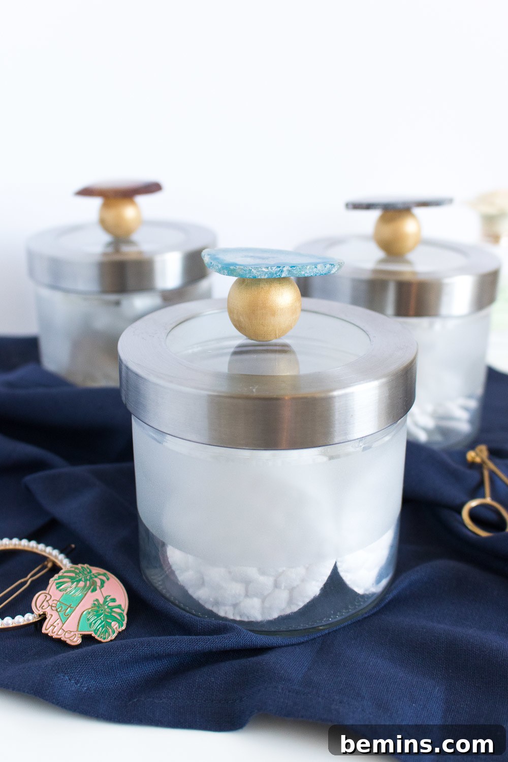 Three glass canisters adorned with agate slices and wooden beads, resting on a navy blue towel.