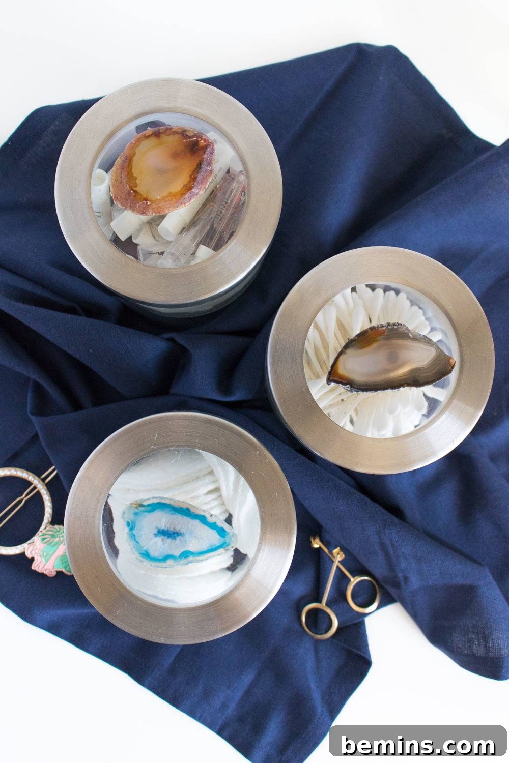 The finished DIY gemstone canisters displayed on a shelf in a bathroom, filled with cotton swabs and other supplies.