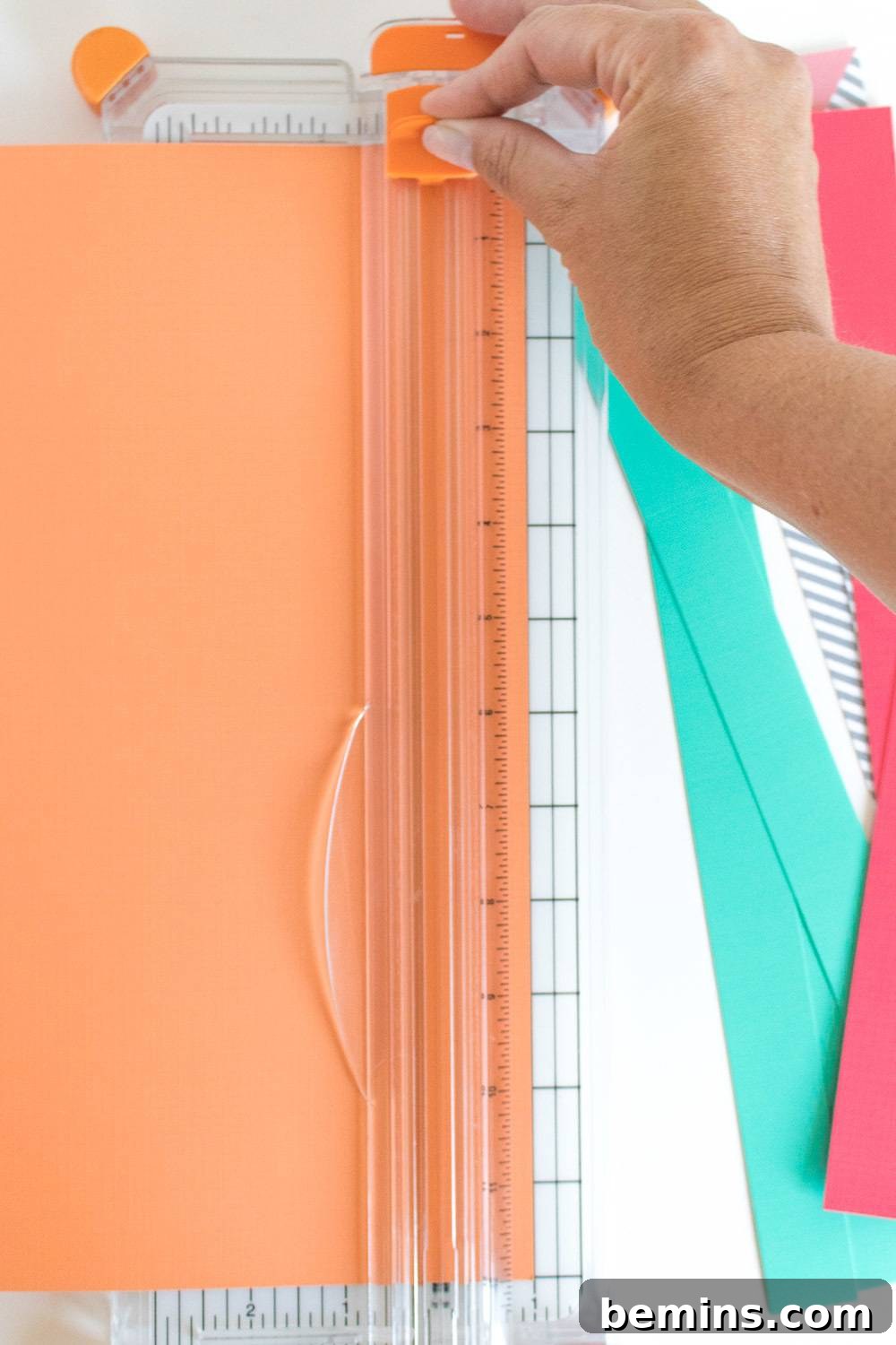 A hand uses a cutting object with orange construction paper in it.