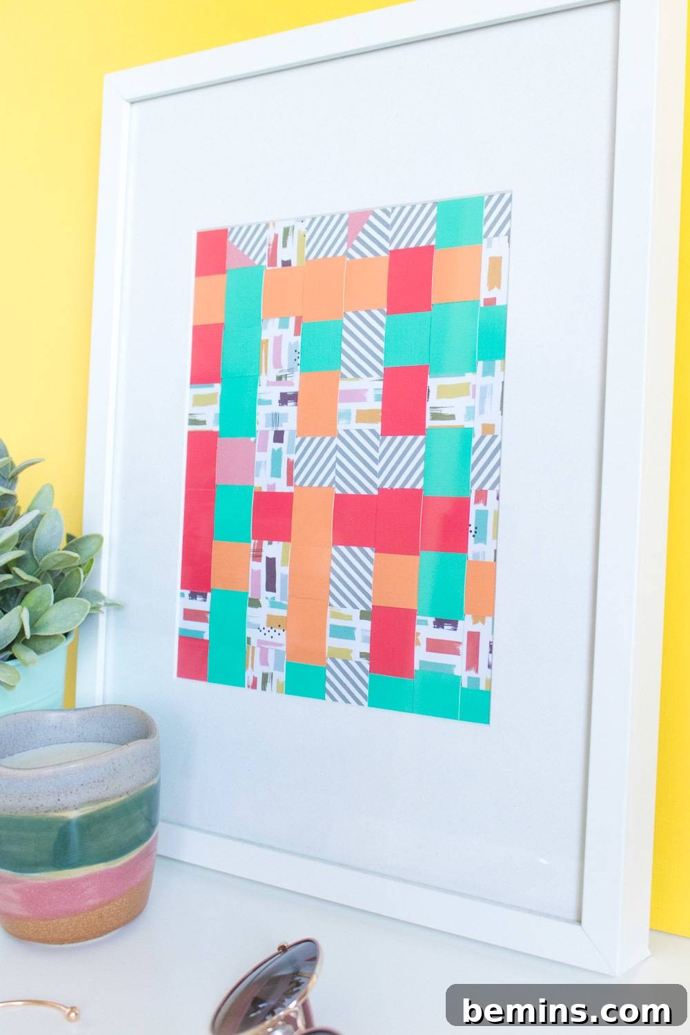 Wall art on woven paper frame and potted plant on table.