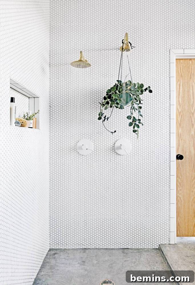 17 Stunning Bathrooms That Embrace the Shower Plant Trend 16 Green shower plant hanging from a golden shower head in a white bathroom.