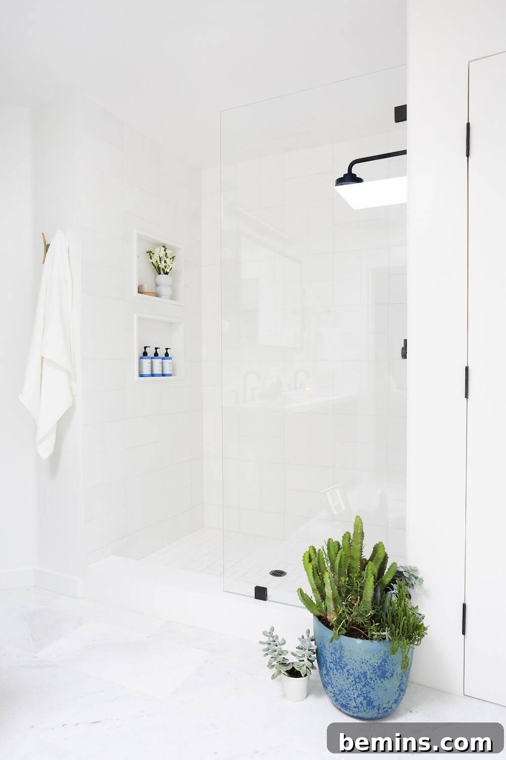 17 Stunning Bathrooms That Embrace the Shower Plant Trend 7 A white shower with a white towel hanging on the wall and two plants, one in a blue planter and one in a tiny white planter next to the shower.