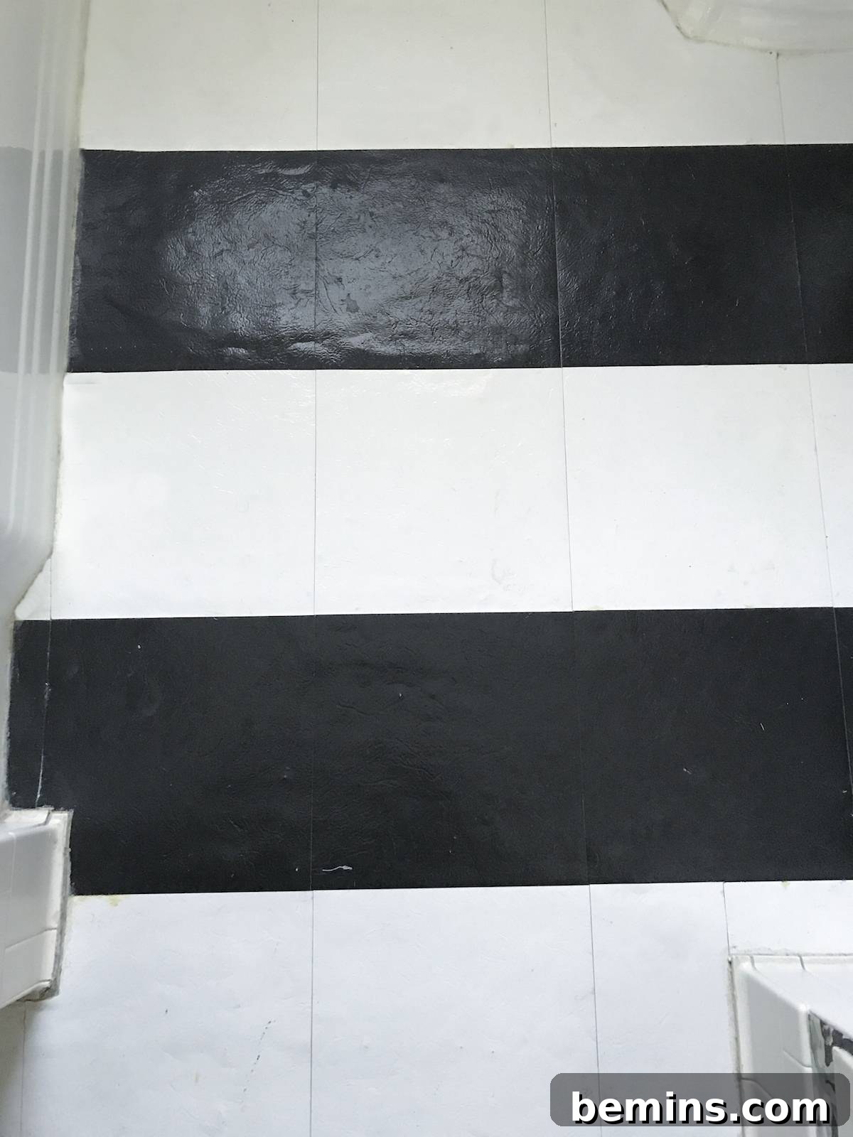 Applying peel-and-stick vinyl tiles to create a striped pattern on the bathroom floor.