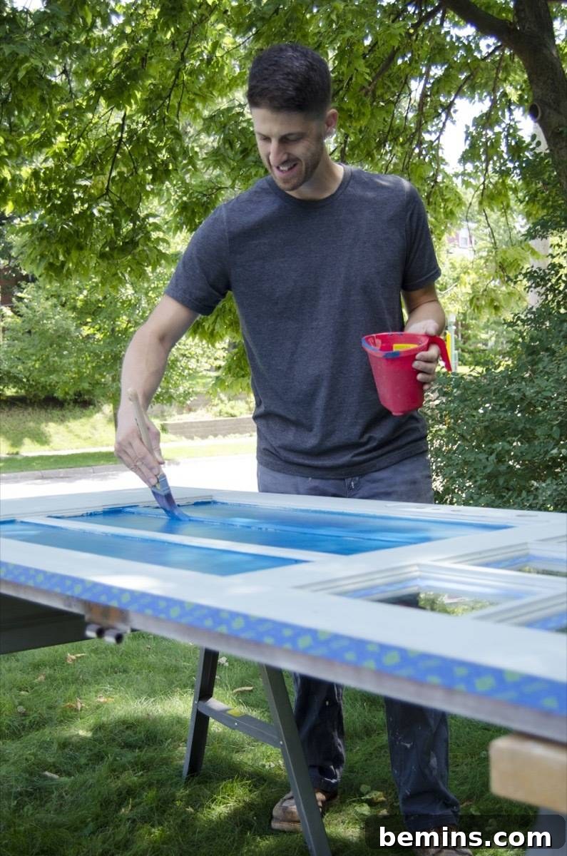 A man diligently applying blue paint to the interior panels of a door resting horizontally on a work table.