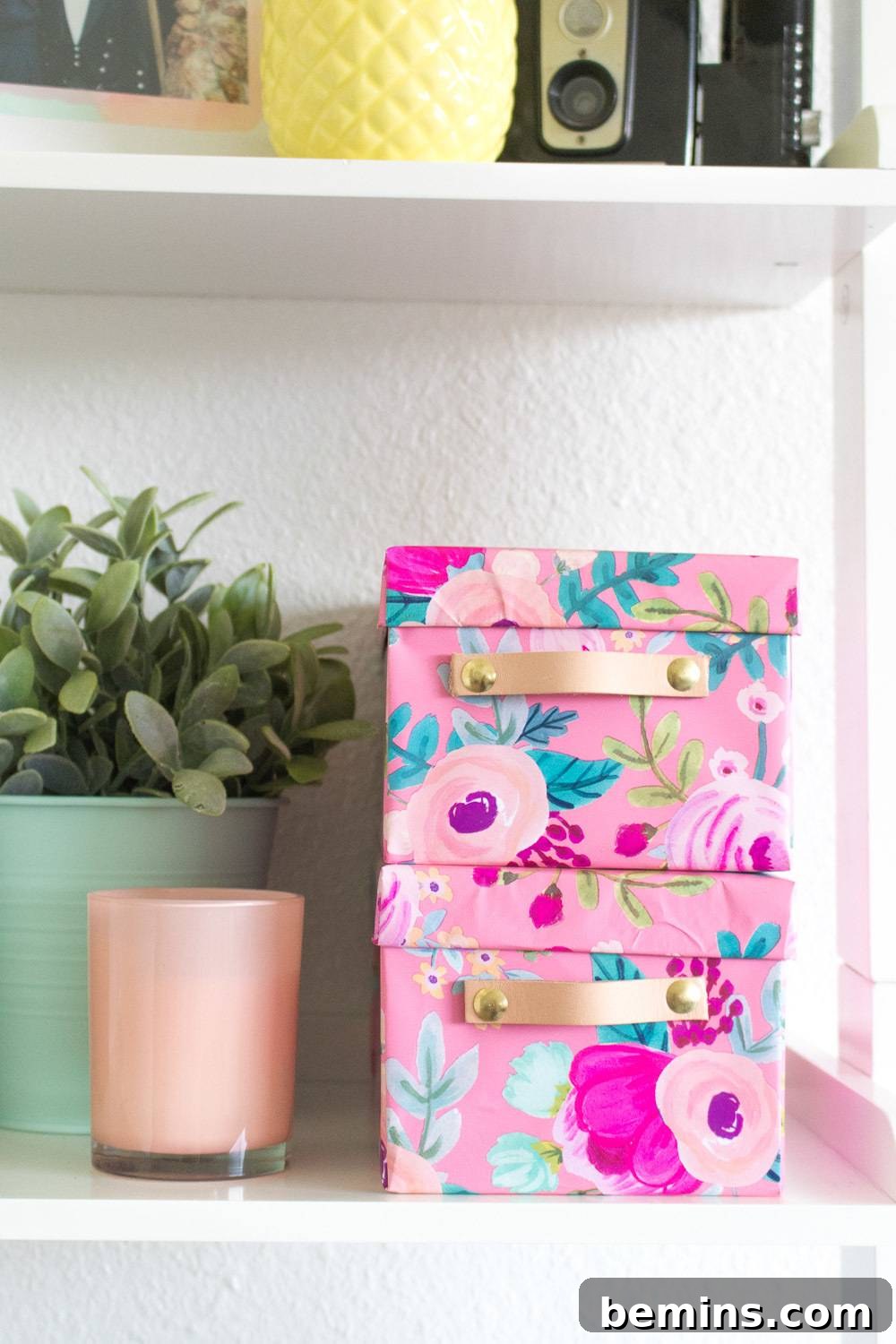 15 Genius IKEA Bedroom Hacks for a Seasonal Home Update 13 A white shelf has pink colorful boxes, a candle and a plant.