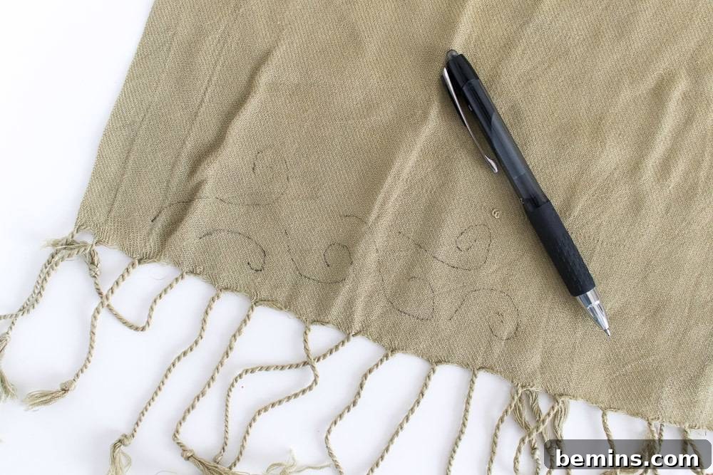 A black pen resting on a brown fabric with delicate markings for embroidery