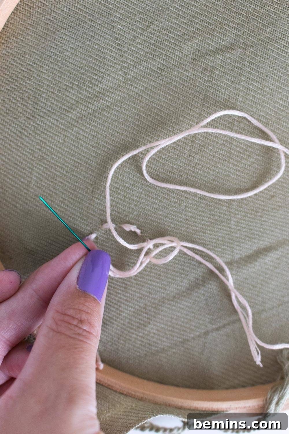 A person with purple fingernails expertly working with embroidery string and needle