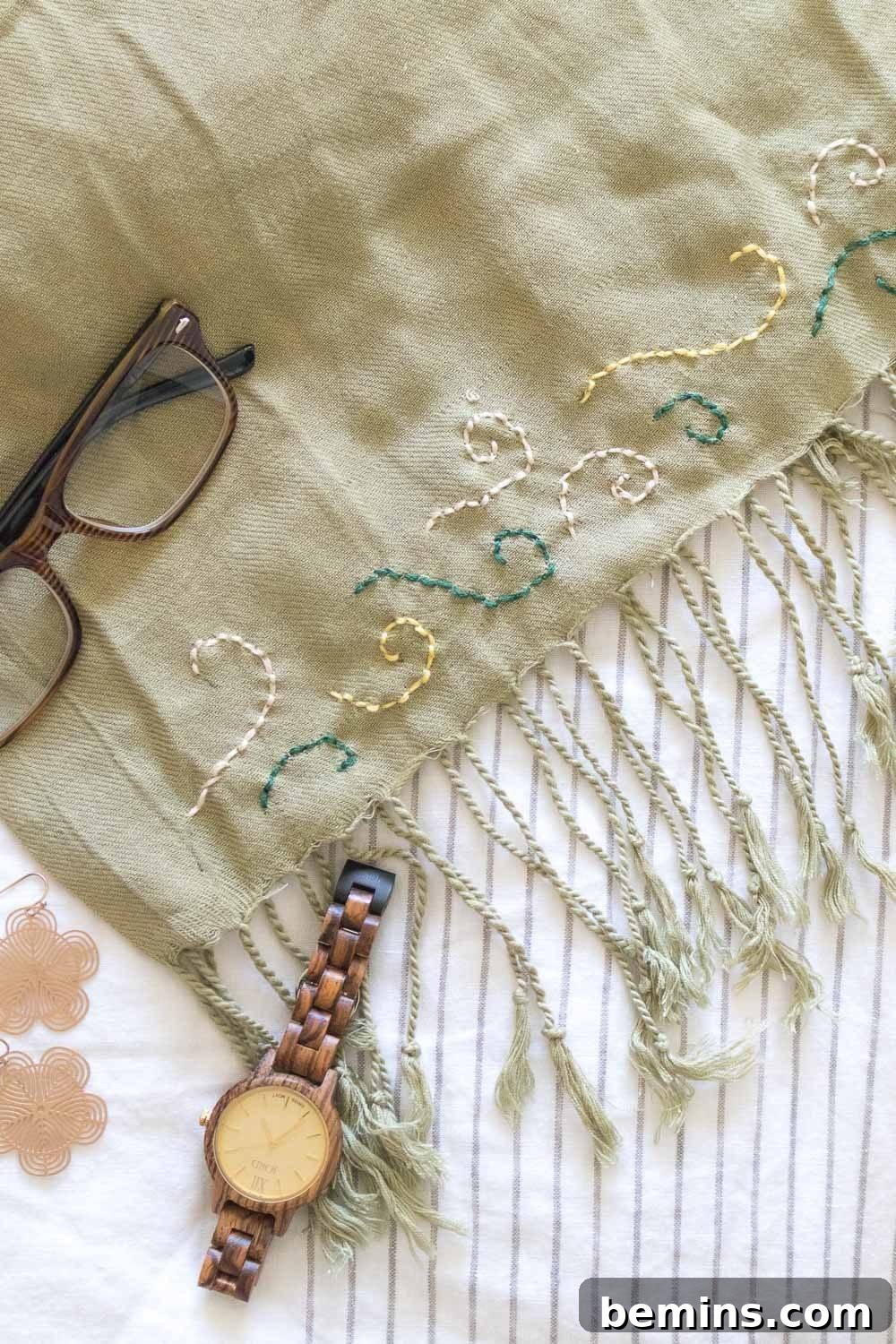 A beautifully embroidered light green scarf with glasses and a watch resting on it, showcasing the finished product