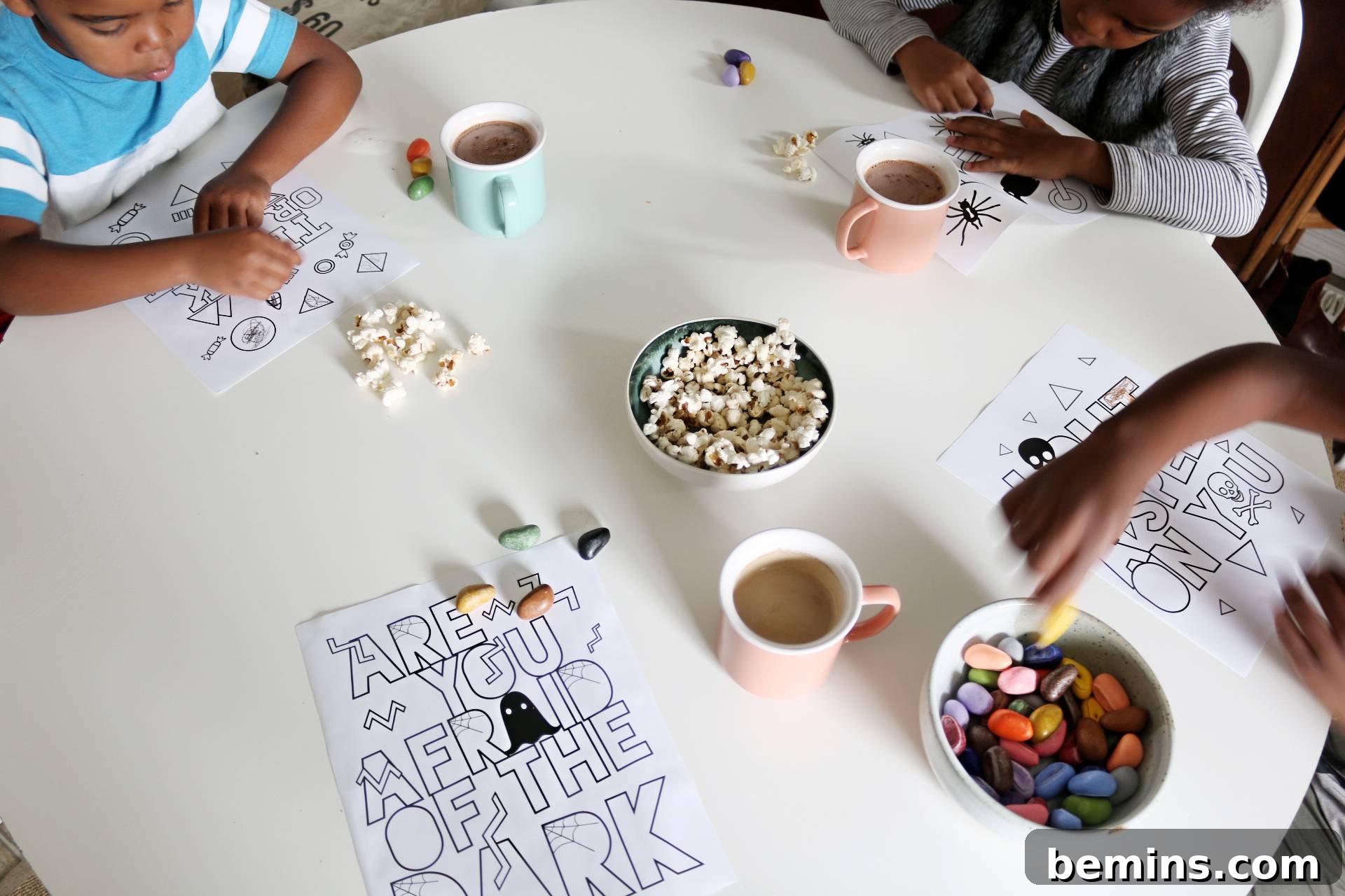 Children coloring Halloween pages at a table with chocolate milk and popcorn, illustrating a family activity