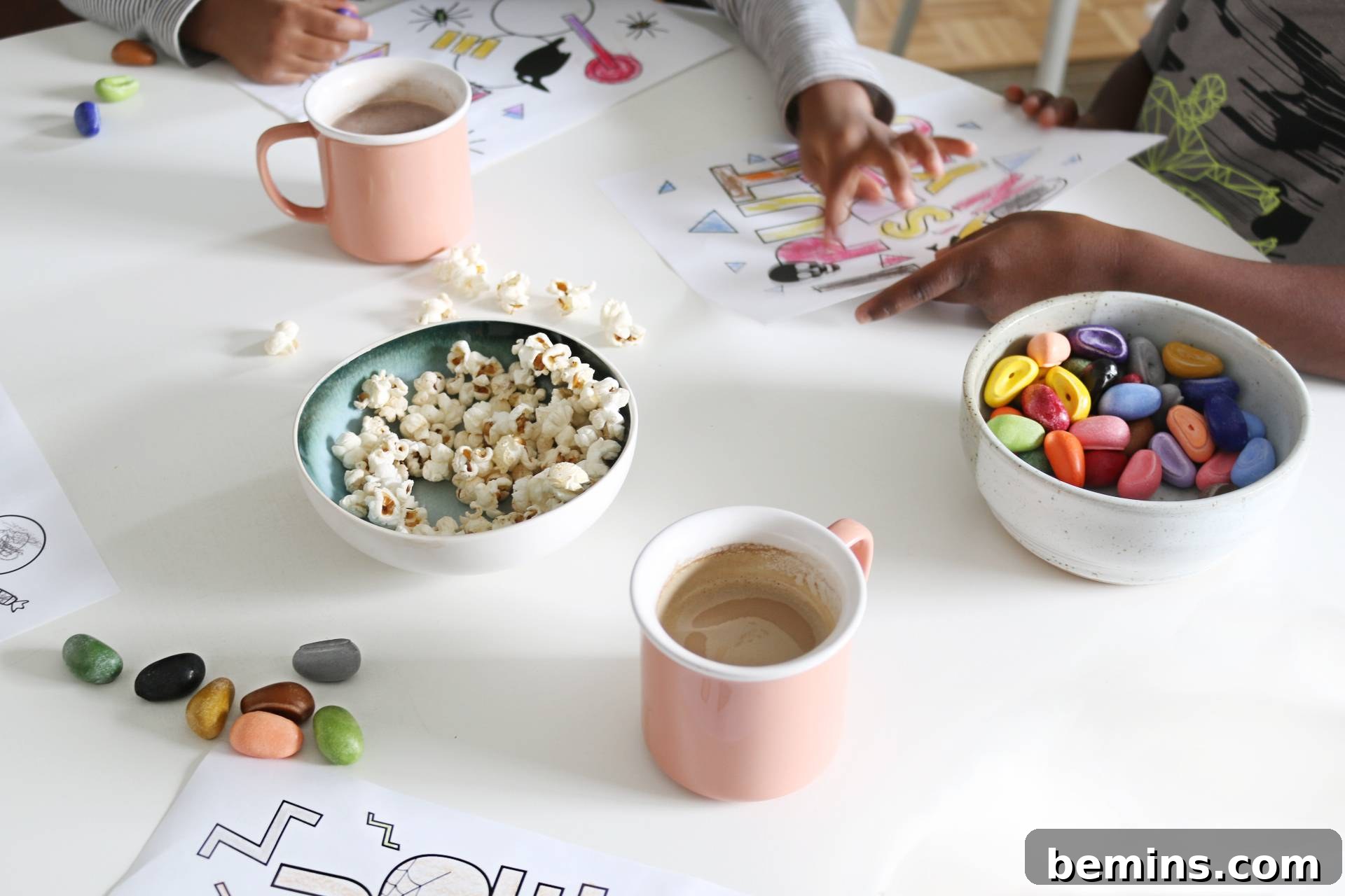 Close-up of popcorn, candy, and mugs of hot cocoa on a table next to Halloween coloring pages, showcasing a festive family setting