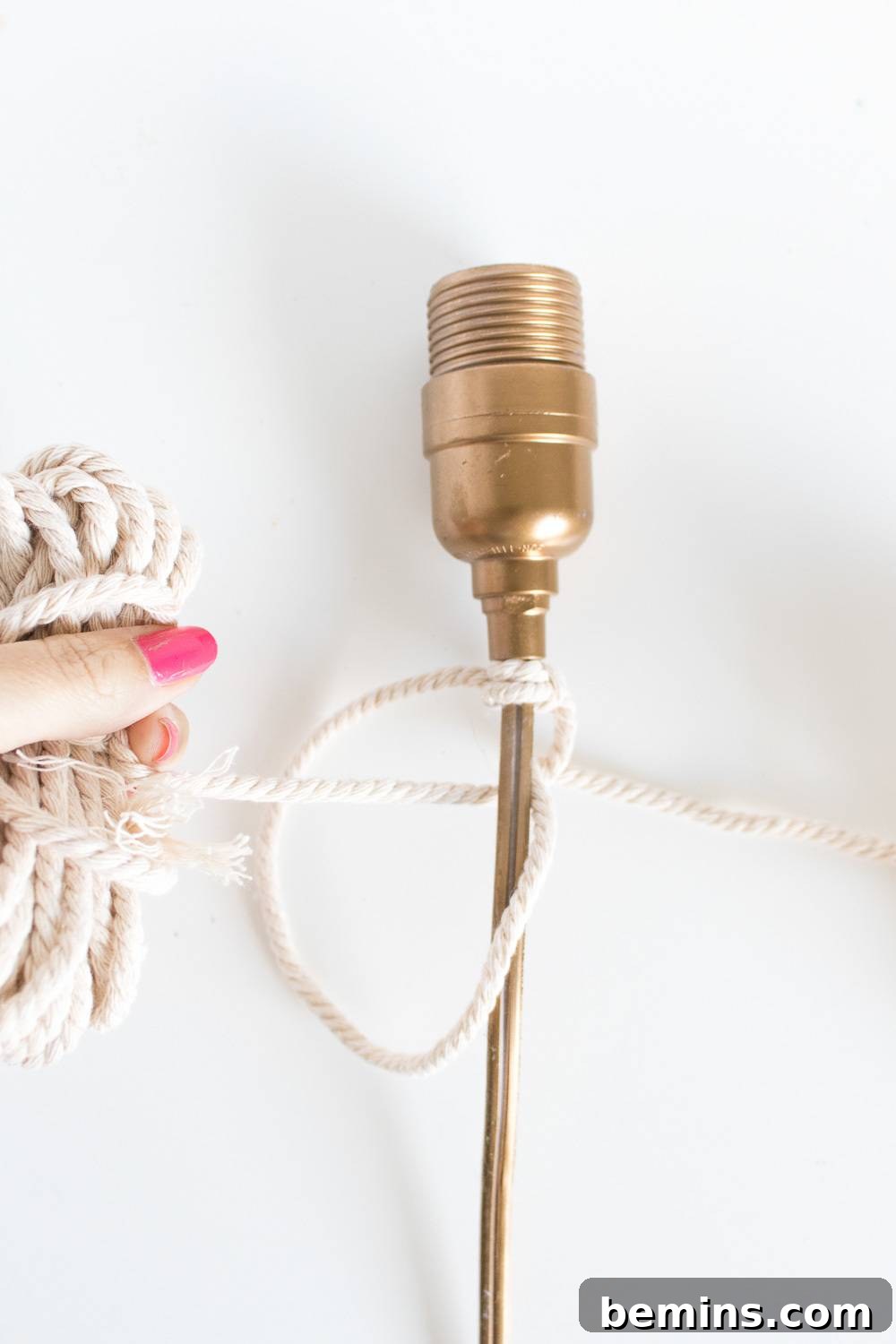 Close-up image of tying the first macrame knot around the lamp base, demonstrating the starting point of the project.