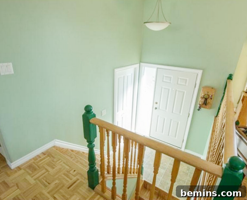 A stairwell with a brown banister and green walls. Before the renovation, the hallway featured outdated mint green walls and standard lighting.