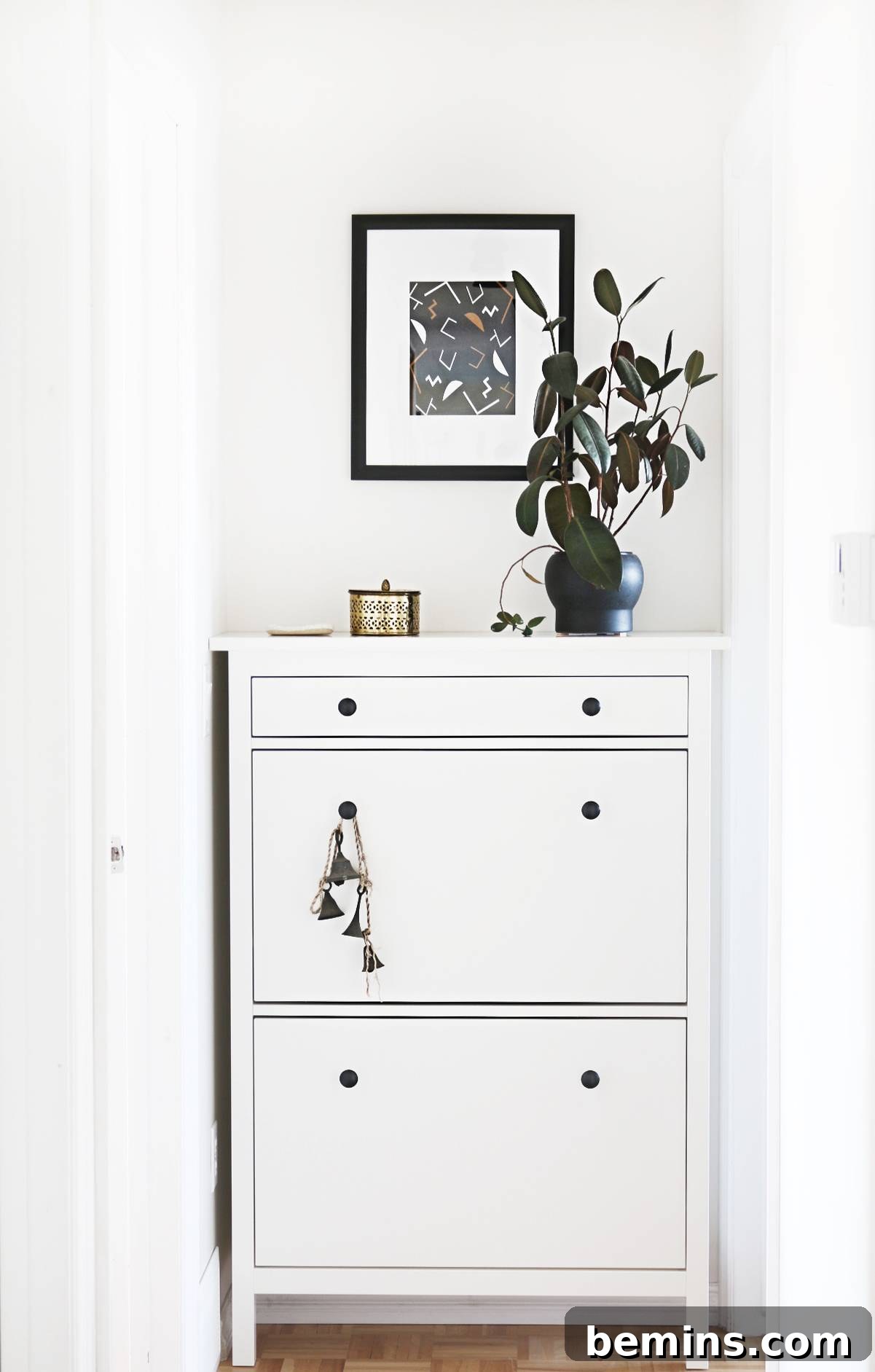 A white dresser has a vase of flowers with a picture above it. A white dresser adds storage and style to the renovated hallway.