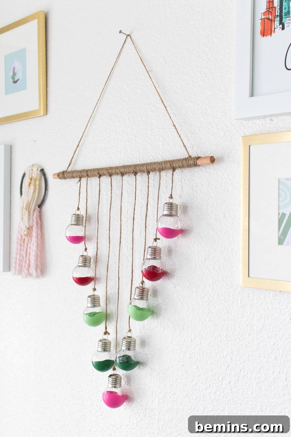 A beautifully crafted wall hanging featuring round Christmas ornaments suspended from a wooden dowel, displayed amongst framed artwork.