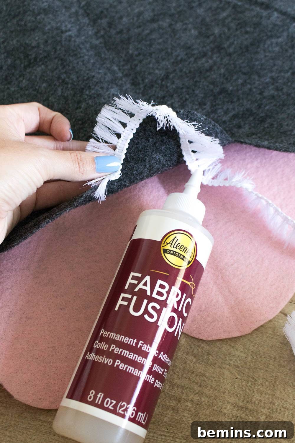Hands applying white fringe to pink fabric with fabric glue, a delicate crafting step