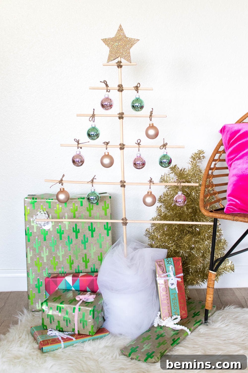 A small golden Christmas tree has hanging ornaments and presents under it.