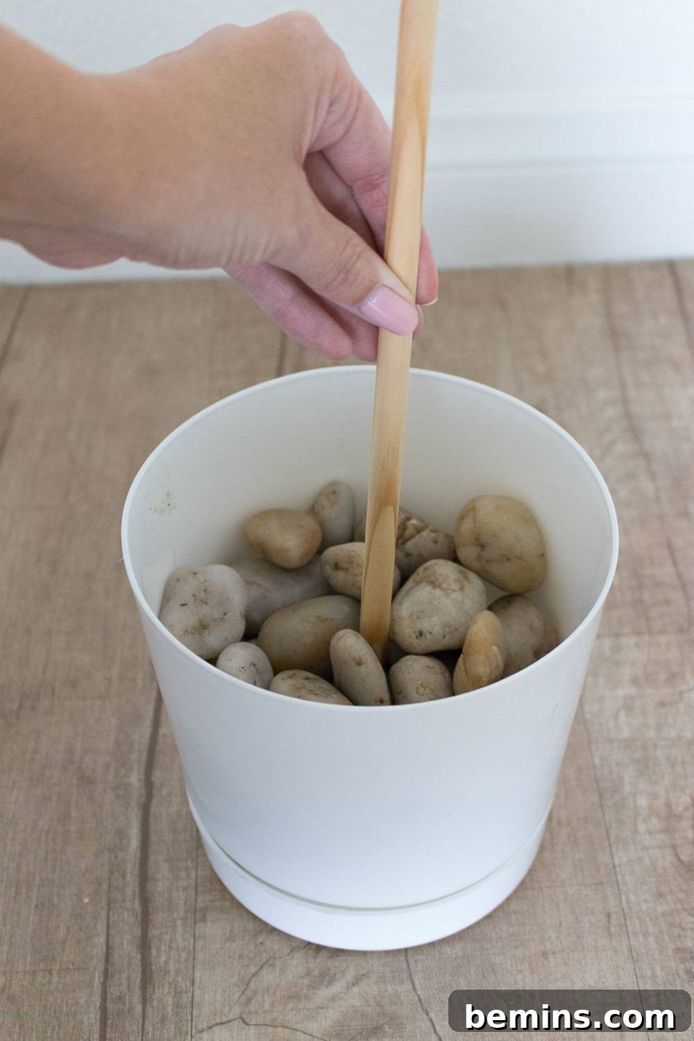 A person putting a stick in a cup of rocks.