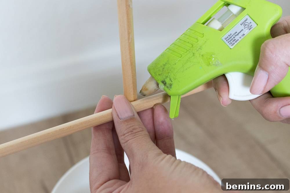 A person using a green glue gun on two dowel rods.