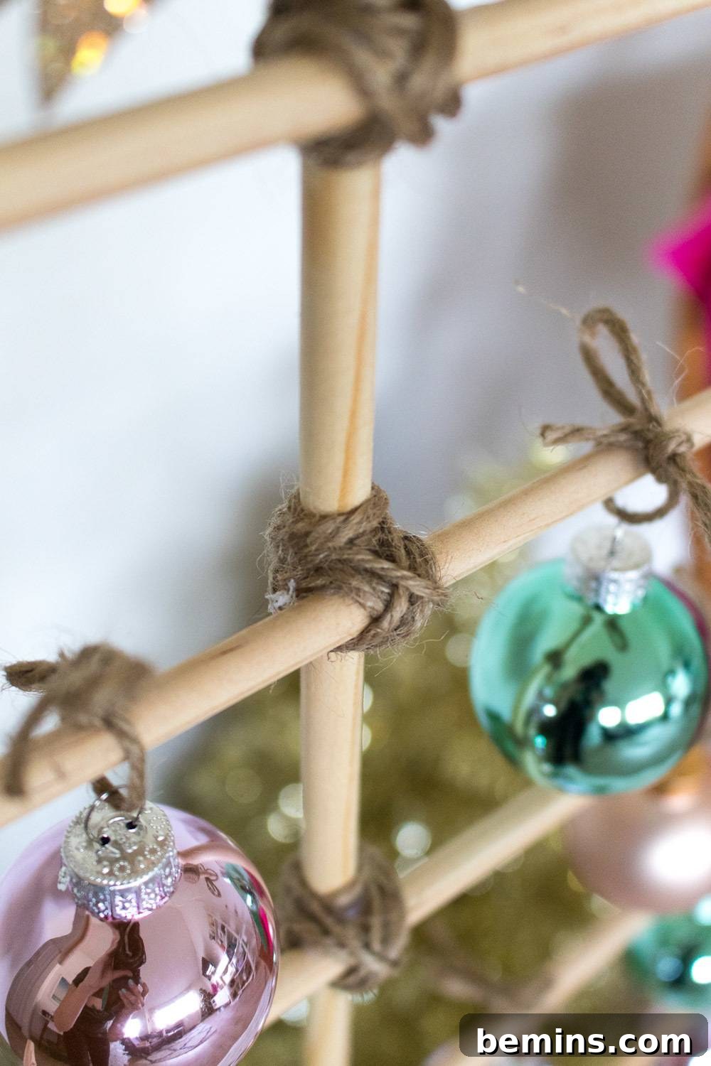 Shiny pink, and turquoise Christmas tree balls are tied to wooden dowels.