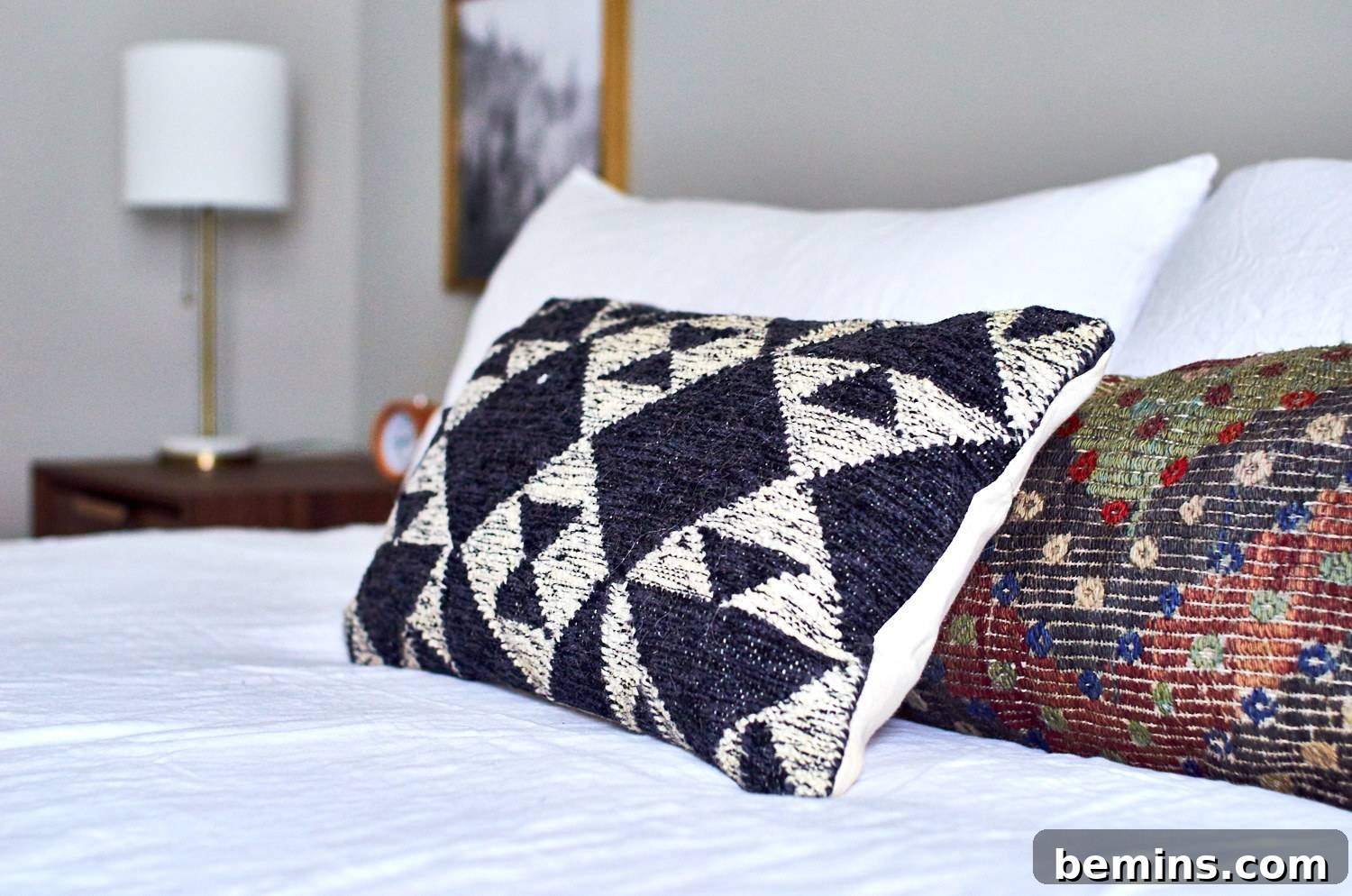 Designer pillows arranged on a bed beside a white-colored table lamp in the bedroom. Thoughtful details and stylish accents enhance a bedroom's ambiance.