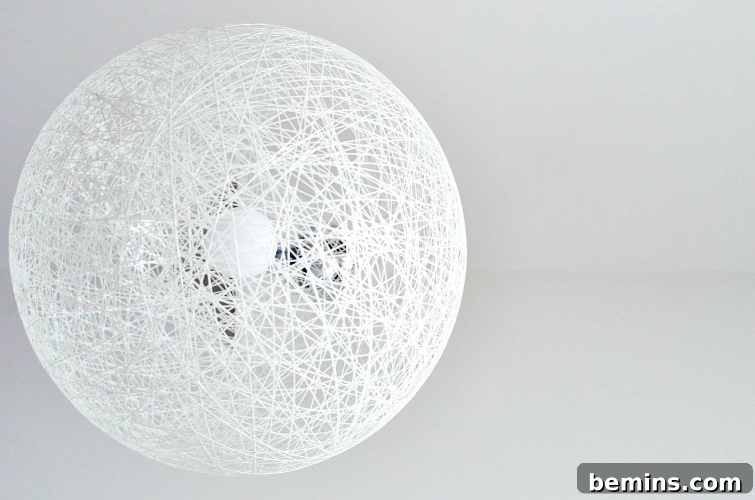 A modern light fixture featuring a spherical design made of interwoven white strands. A statement pendant lamp enhances a room's contemporary design.