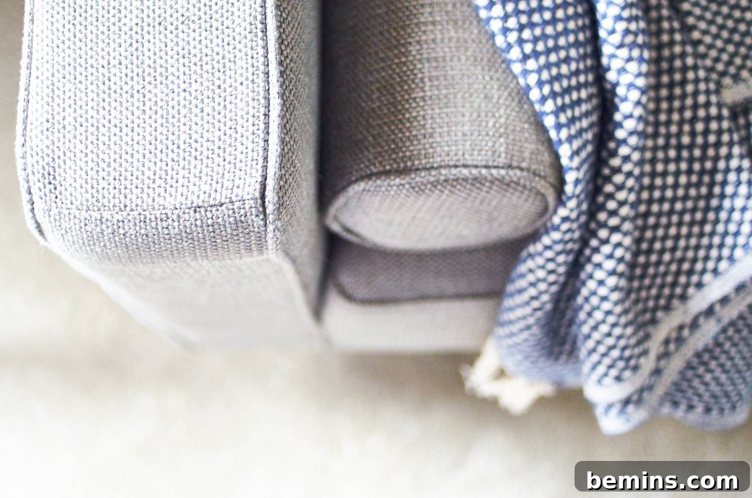 A close-up shot of a gray couch adorned with a blue and white checkered blanket featuring fringe. The soft textures and neutral color palette bring the space together.