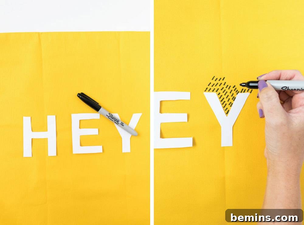 A person using a marker on a yellow background with white letters. The process of creating the typographic pillow.