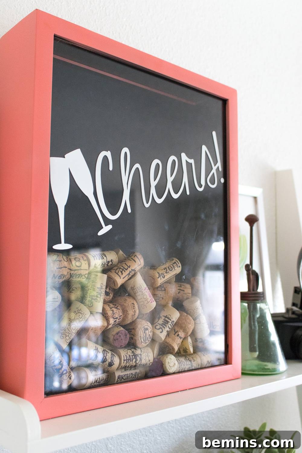 Corks being placed into a red-framed memory box with the word 'Cheers' on it.