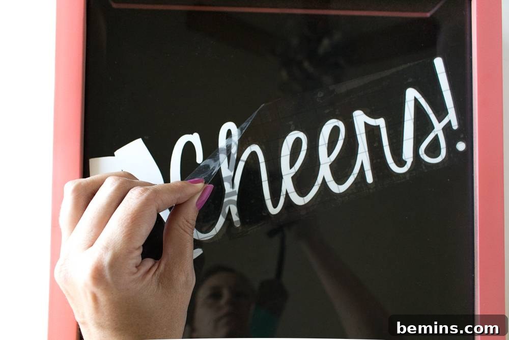 A woman removing transfer tape to reveal a custom word applied to a picture frame.