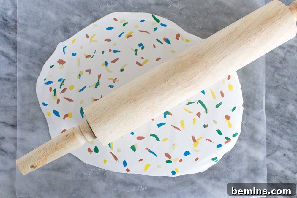 A wooden rolling pin laying on a multi colored rolled out dough on a grey marble surface.