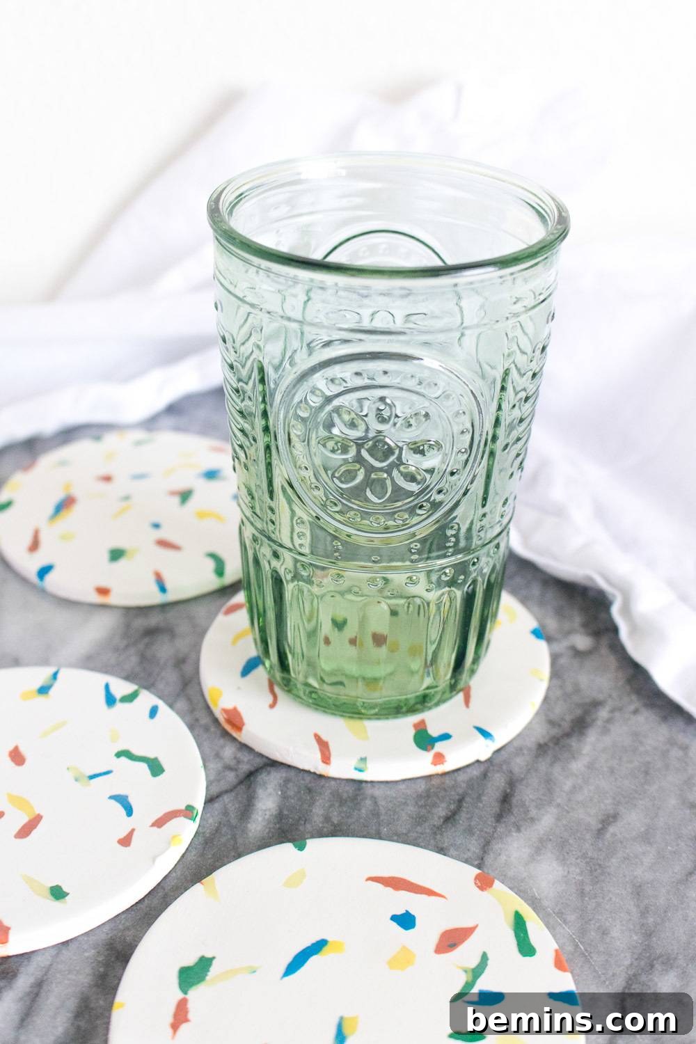 A clear glass is sitting on a white coaster with colorful dots.
