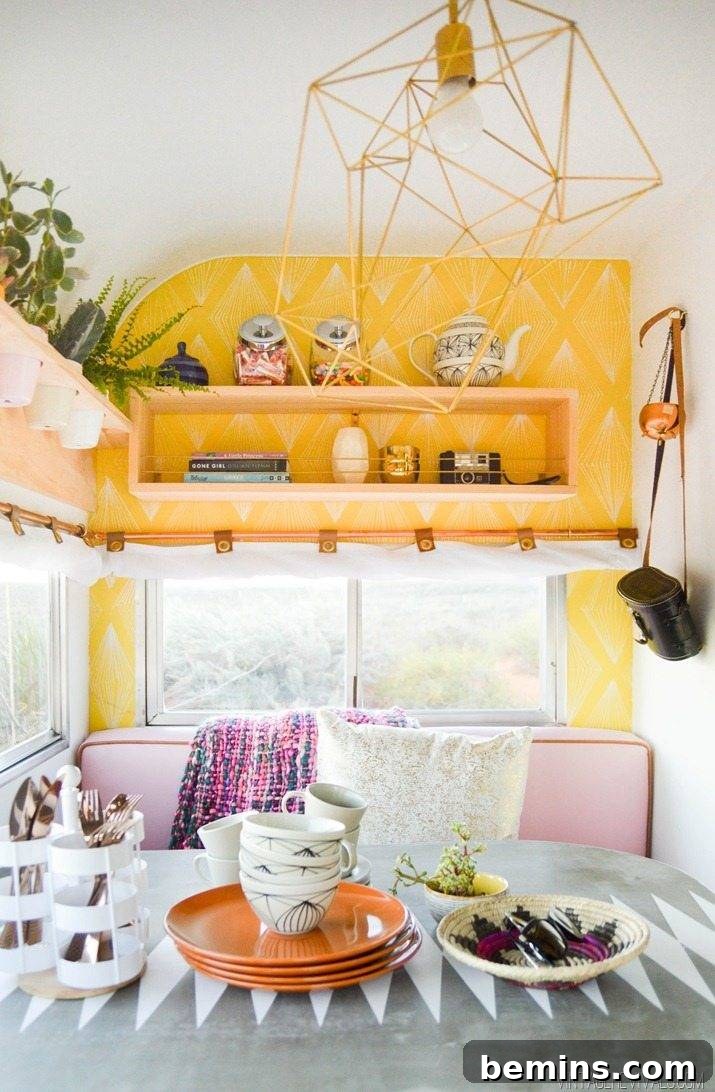 The interior of a remodeled camper, featuring yellow shelves, a pink couch, and a grey table set with orange plates.