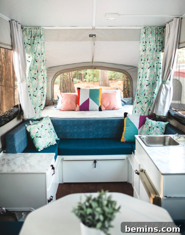 The interior of a pop-up camper remodel, featuring faux marble accents, new flooring, and colorful curtains.
