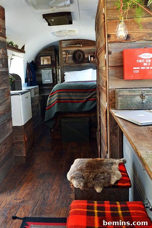 The tidy and rustic interior of a renovated Airstream trailer, showcasing reclaimed wood accents and red plaid stools.