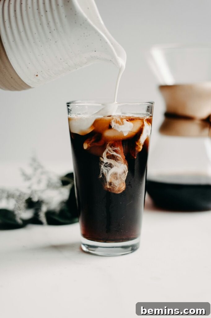 Iced coffee with creamer being poured from a pitcher.