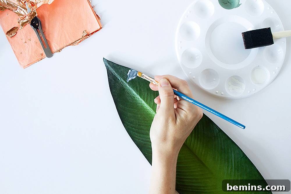 Applying gilding adhesive to a faux plant leaf with a foam brush.