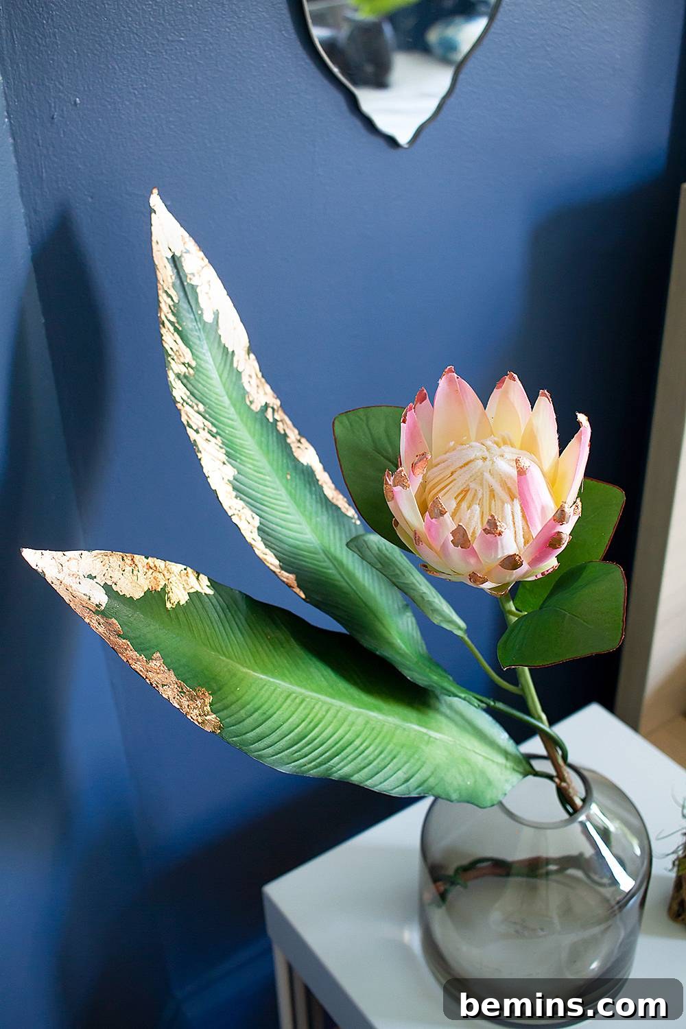 Pink and white flower arrangement in a glass vase, enhanced by copper leaf accents.
