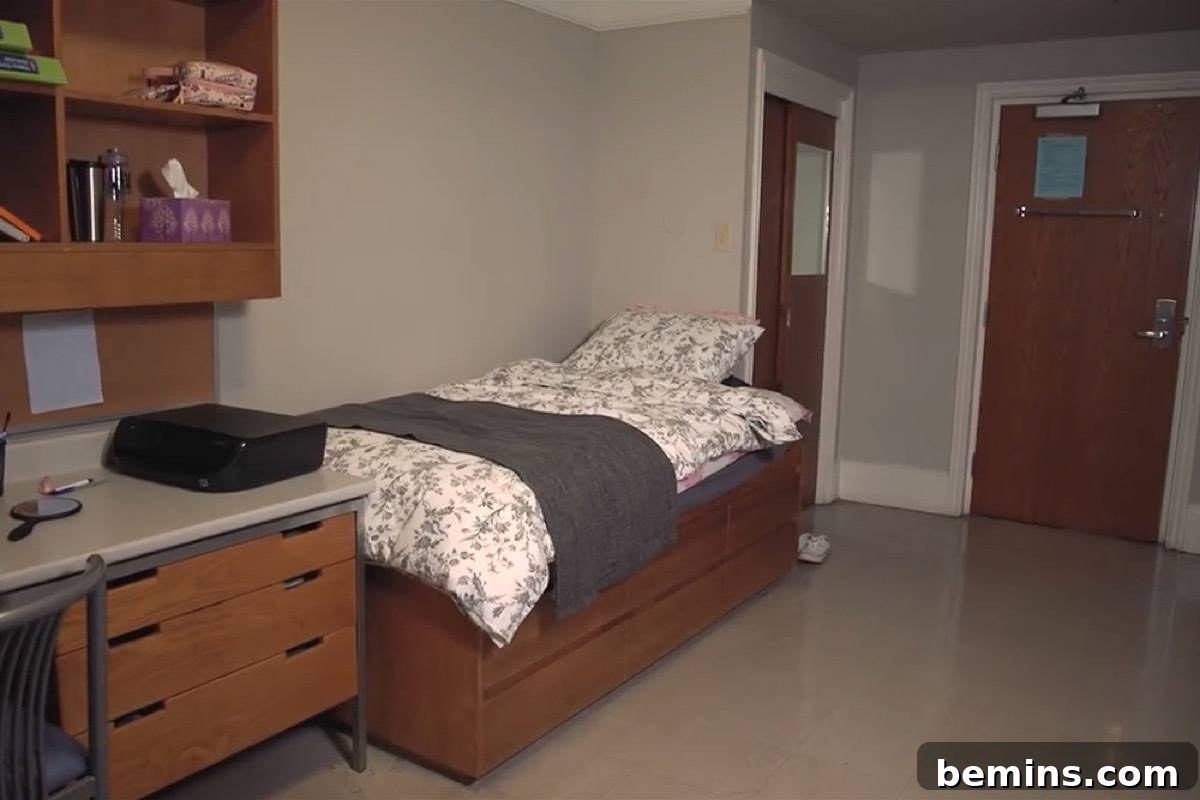 Before: A dorm room with a made bed, a dark grey throw blanket and a tidy desk with shelves above it.