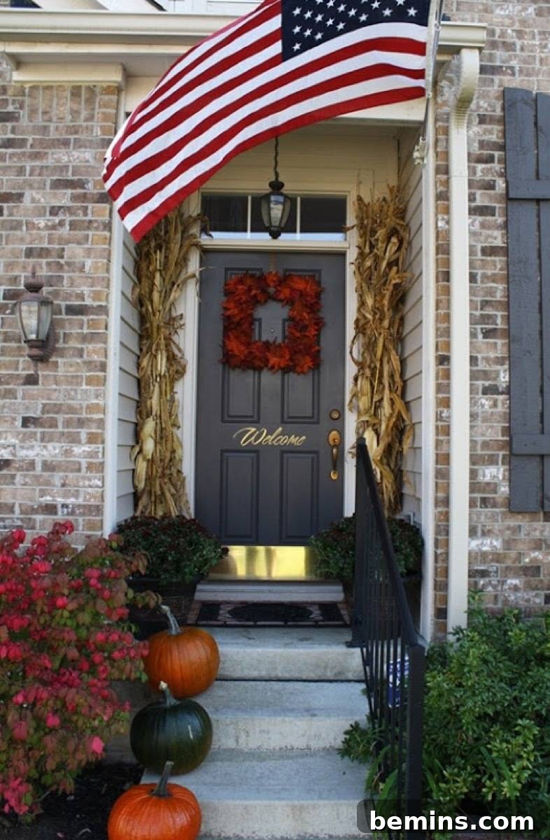 A fall front porch adorned with pumpkins, cornstalks, and a square red wreath, creating a warm and inviting atmosphere