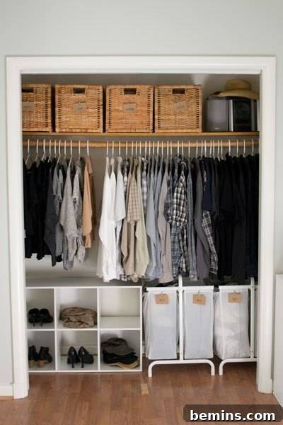 An organized closet with woven baskets on the top shelf, clothes hung in the middle, and white shoe boxes and laundry hampers on the bottom.
