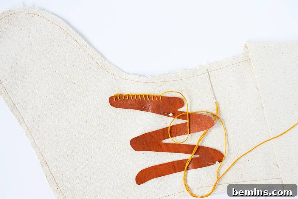 Leather monogram stocking being stitched together with yellow string on top of a white table.