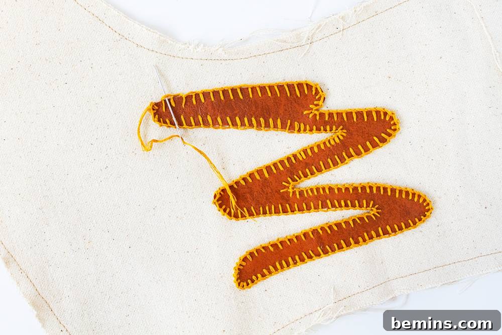 A brown squiggly design that has been stitched onto a white t-shirt with yellow stitching.