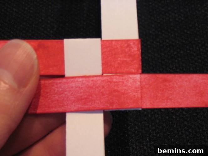 A person is holding red and pink strips of paper. Locking the strips ensures the star stays together.