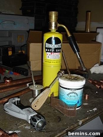 Unleash Your Inner Craftsman: Mastering the Art of Copper Pipe Soldering 3 A collection of tools required for copper pipe soldering, including a gas tank, copper wires, a vise grip, and other assorted items on a workbench.