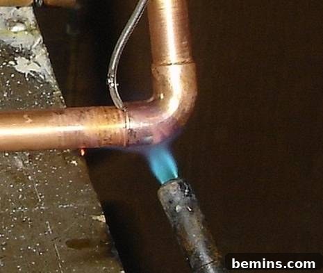 Unleash Your Inner Craftsman: Mastering the Art of Copper Pipe Soldering 7 A copper pipe being soldered with a torch, demonstrating the application of heat and solder to create a strong, leak-proof joint.