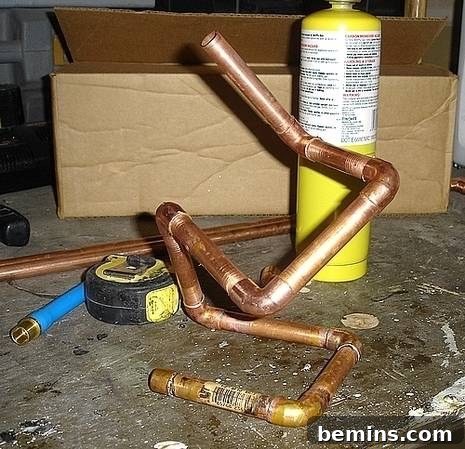 Crafting Copper Art Projects with New Soldering Skills 8 A butane torch and measuring tape laid next to partially soldered copper pipes and fittings, indicating ongoing work on the sculpture.