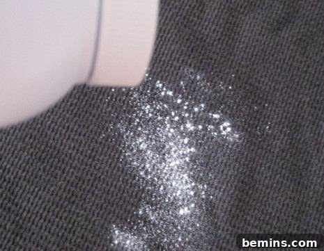 Powder is being sprinkled on a grey surface, demonstrating the application of baby powder onto the stain.